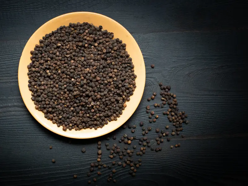 Whole black peppercorns piled on a ceramic plate