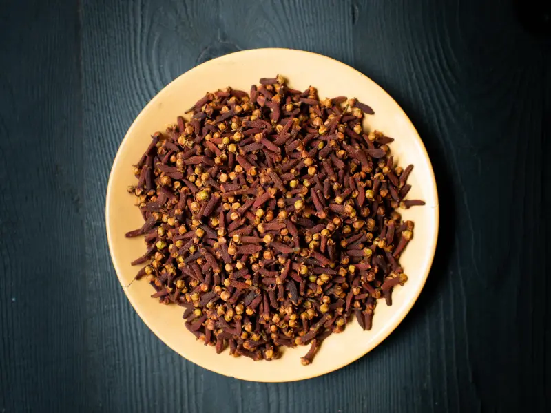 Whole dried cloves piled on a ceramic plate